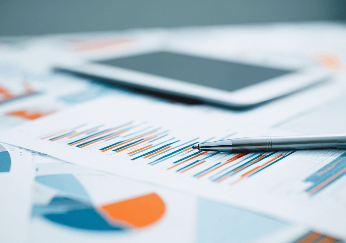 Close-up of financial charts, a silver pen, and a tablet on a desk, perfect for illustrating data analysis or business reporting.