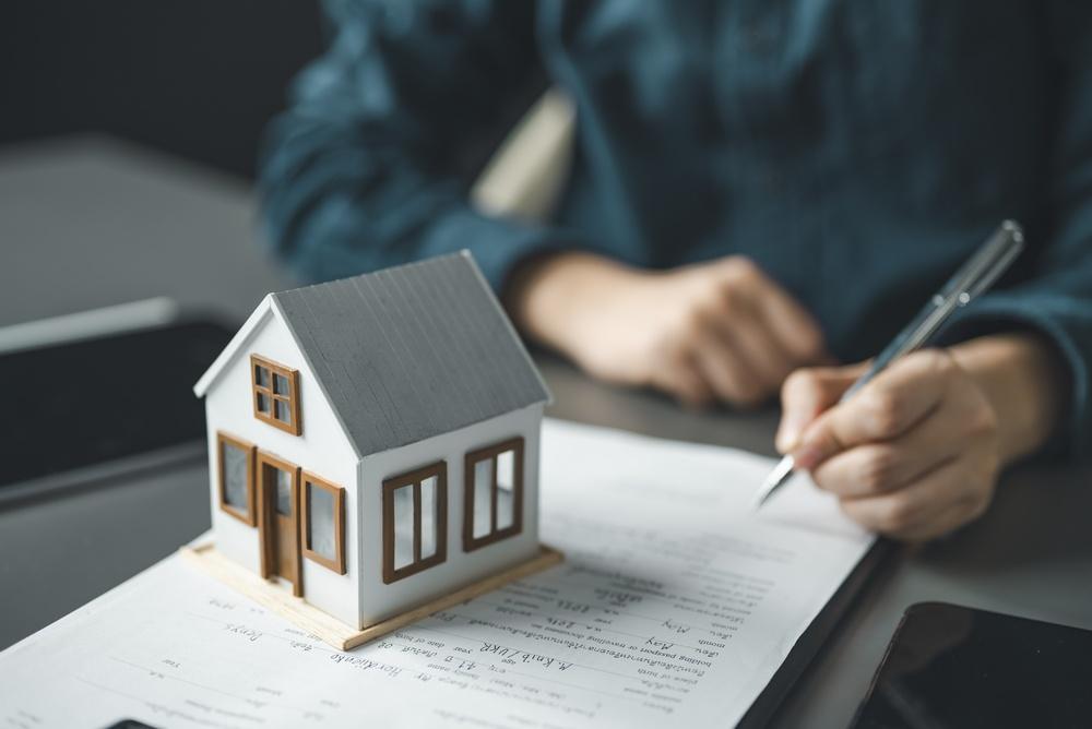 Small model house sitting on top of property tax documents while a person signs paperwork